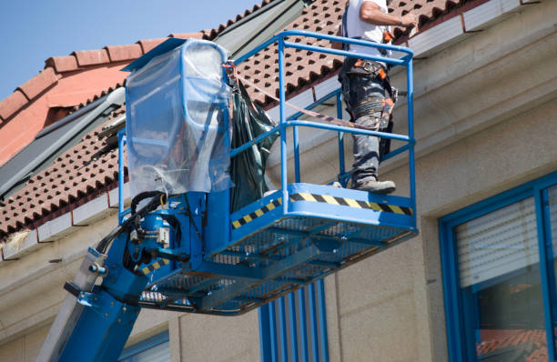 Worker on hydraulic lift repairing house roof gutter to fix gutter leak and ensure proper rainwater drainage.