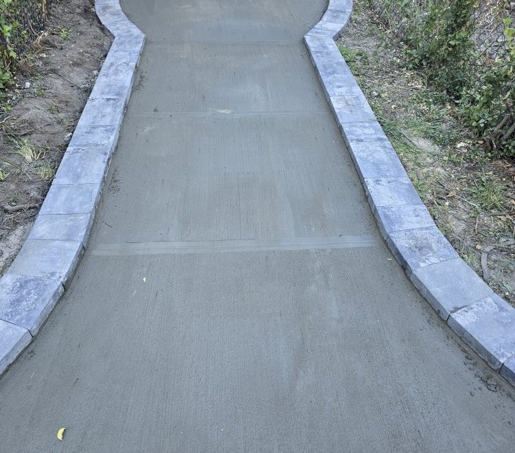 Newly poured concrete walkway with smooth edges, invitingly leading to a home, surrounded by elegant stone pavers.