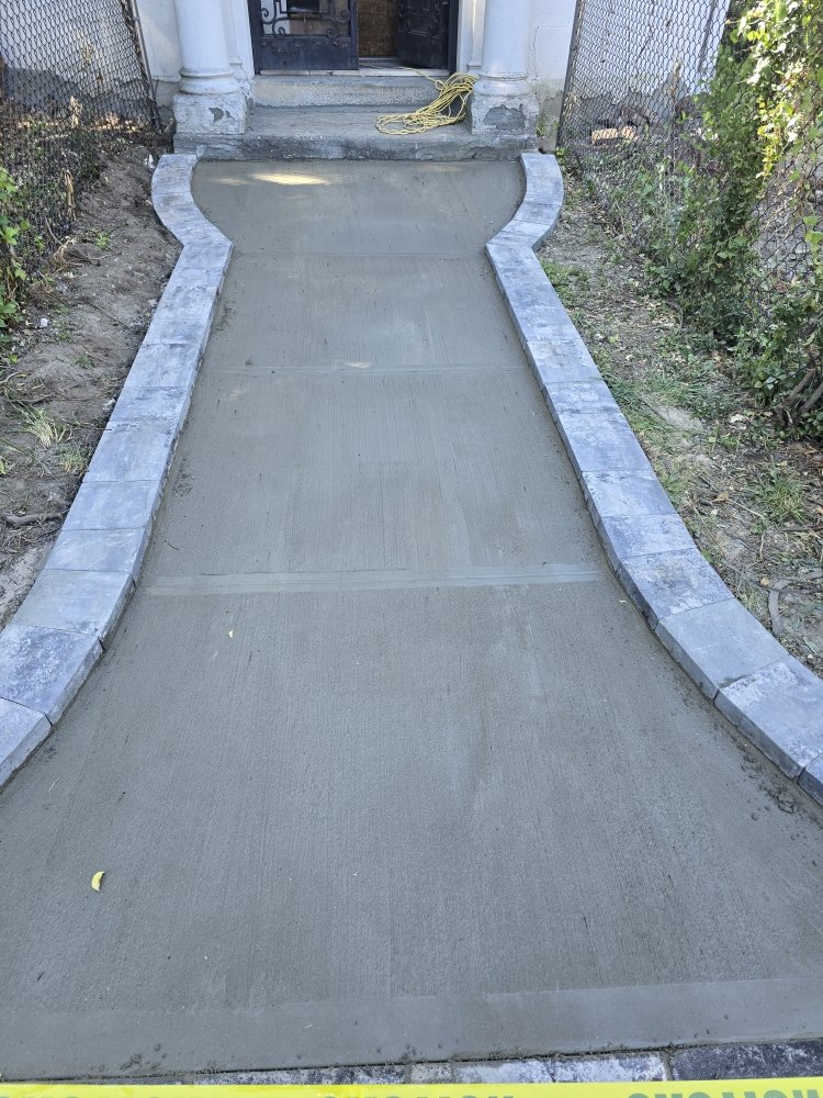 Newly poured concrete walkway with smooth edges, invitingly leading to a home, surrounded by elegant stone pavers.