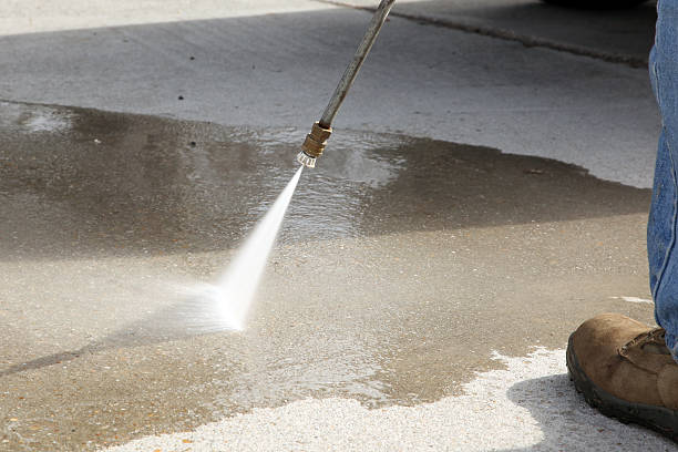 contractor using a power washer to clean a concrete driveway surface