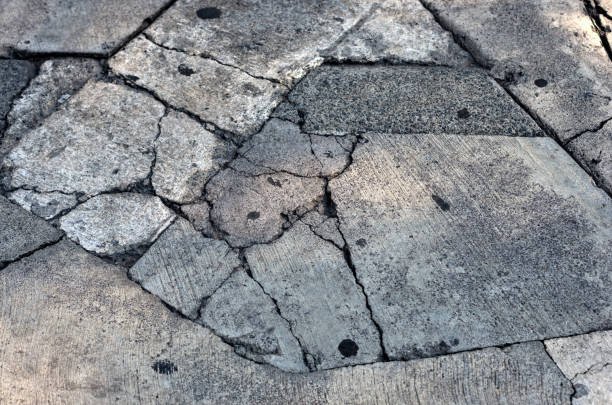 Close-up of damaged concrete driveway with severe cracks and patch repairs