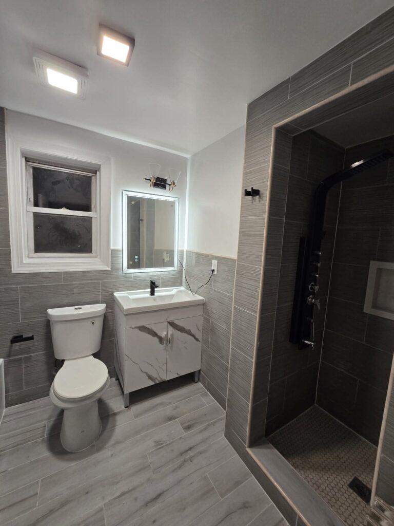 Modern small NYC bathroom with toilet, vanity, and walk-in shower showcasing efficient use of compact space.