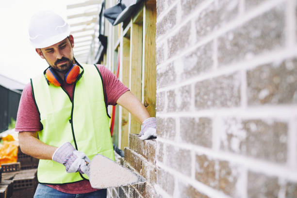 Skilled construction worker with bricks and mortar, wearing safety gear, carefully laying bricks to build a strong wall in NYC.