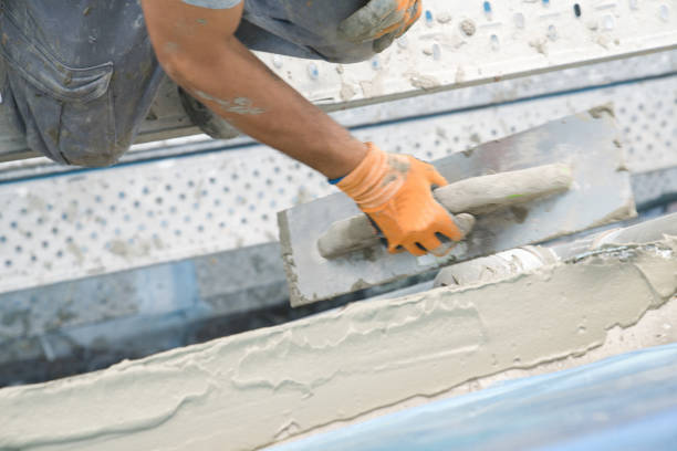 Worker applying waterproof coating on concrete surface with a trowel to prevent water damage.