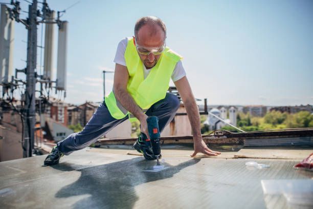 Worker in safety gear drilling on a flat roof durWorker in safety gear drilling on a flat roof during replacement project under clear sky.ing replacement project under clear sky.