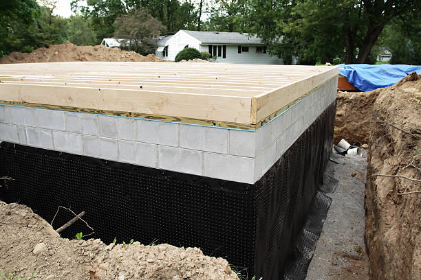 New home foundation walls sealed with black waterproofing membrane to prevent water seepage and protect basement.