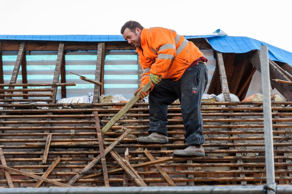 Worker removing old roofing materials during a shingle roof replacement project.