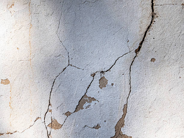 Stucco wall with visible hairline cracks and peeling due to settlement and moisture damage