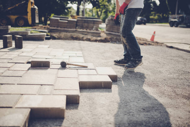 Worker installing brick paver sidewalk blocks for a durable walkway.