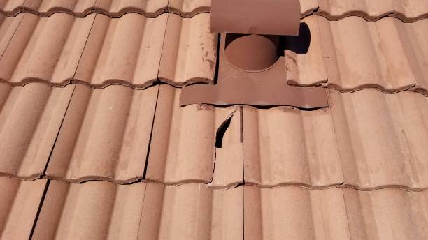 Cracked roof tiles around a vent pipe on a house roof.