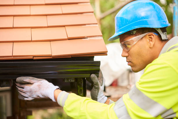 Worker in safety gear performing gutter installation under a tiled roof for improved water flow.