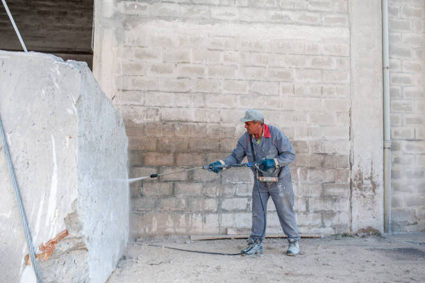 Worker pressure washing paint off a brick wall removing paint from brickwork safely.