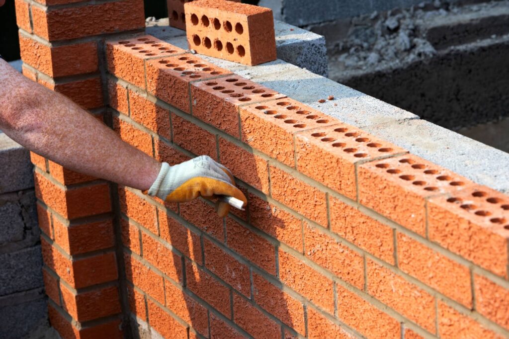 Worker building a brick retaining wall using red clay bricks and mortar