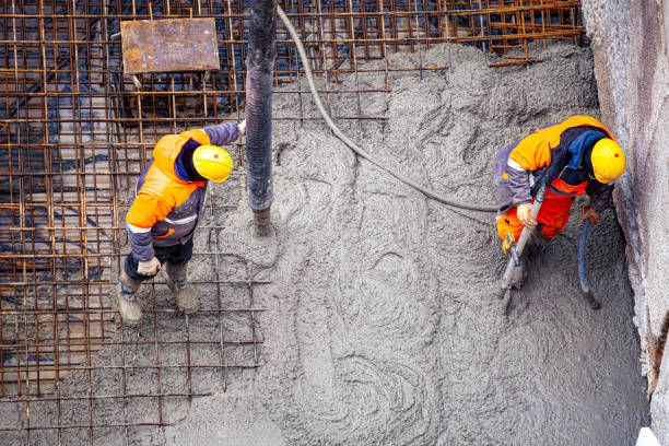 Workers pouring and compacting concrete for reinforced concrete foundations at a construction site.