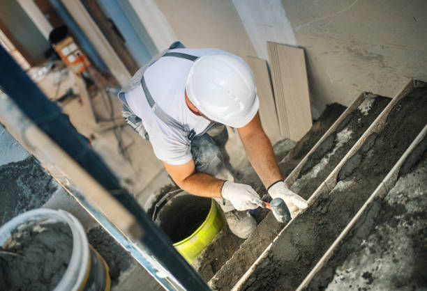 Worker repairing concrete steps using a trowel and fresh concrete mixture at a construction site.
