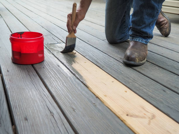 Professional deck painting service with worker applying fresh paint to wooden deck boards for restoration.