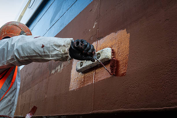 Worker applying exterior waterproofing paint on concrete wall.