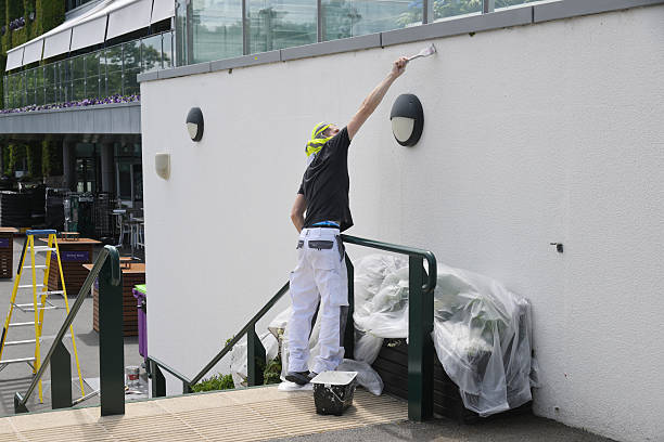 Professional painter applying fresh white paint to an exterior masonry wall