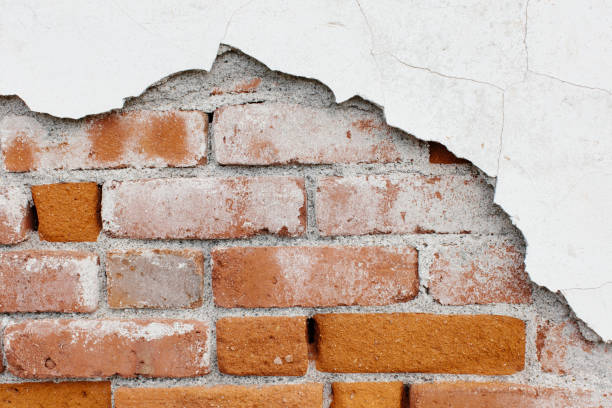 Damaged brick wall with peeling white render showing moisture and structural deterioration