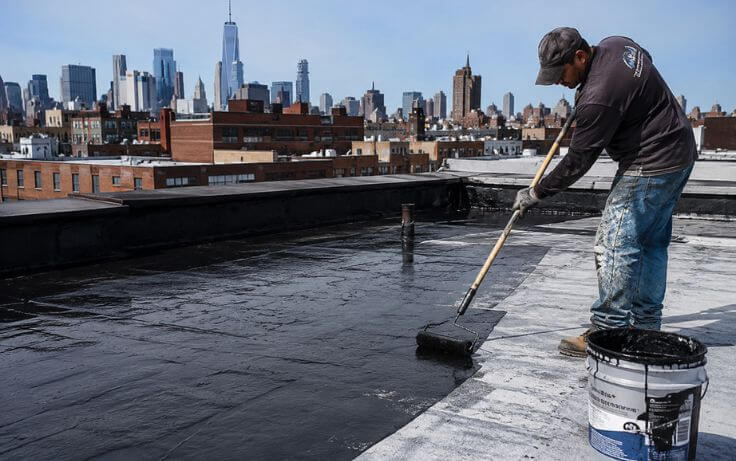 Roof waterproofing contractor applying waterproof coating on a flat roof in NYC to prevent leaks and water damage